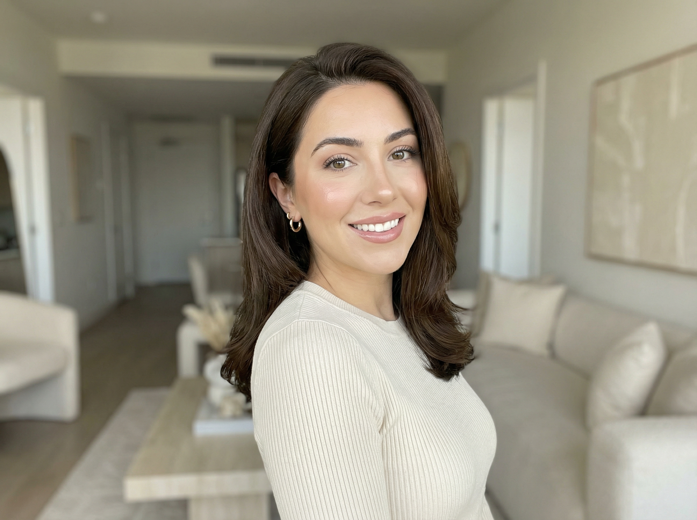 Photoreal portrait of a fictional lifestyle influencer smiling in a bright neutral apartment with a soft creator aesthetic.